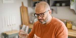 mature adult man in cozy interior of home kitchen  taking medication