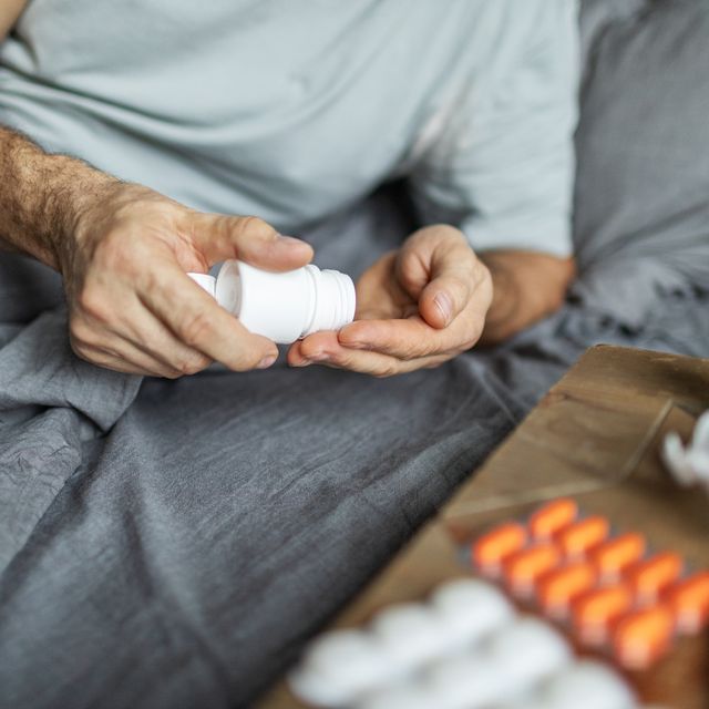 mature adult man lying down in bed and feeling sick, taking pills