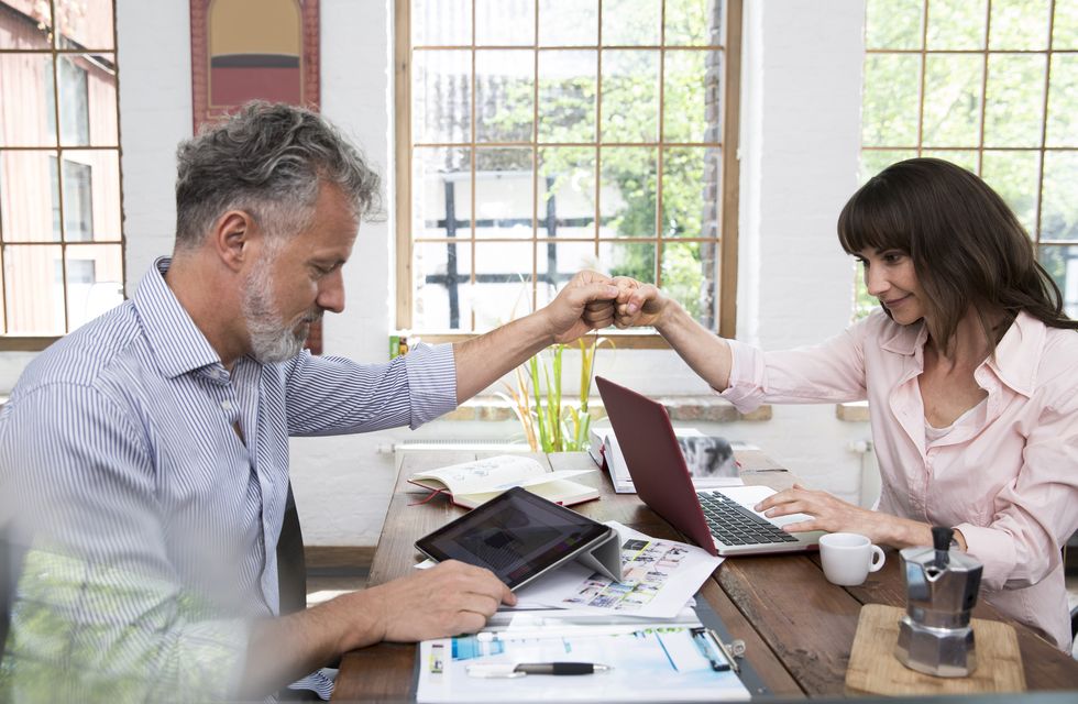 mature couple high fiving in home office, using laptop and digital tablet