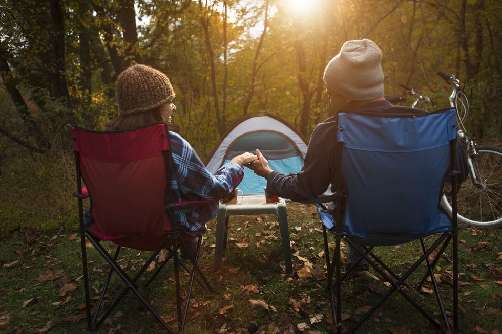 mature couple sitting on camping chairs outside tent, holding hands