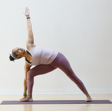 a mature latinx woman with curly dark hair, does the triangle pose wearing yoga clothing in a yoga studio