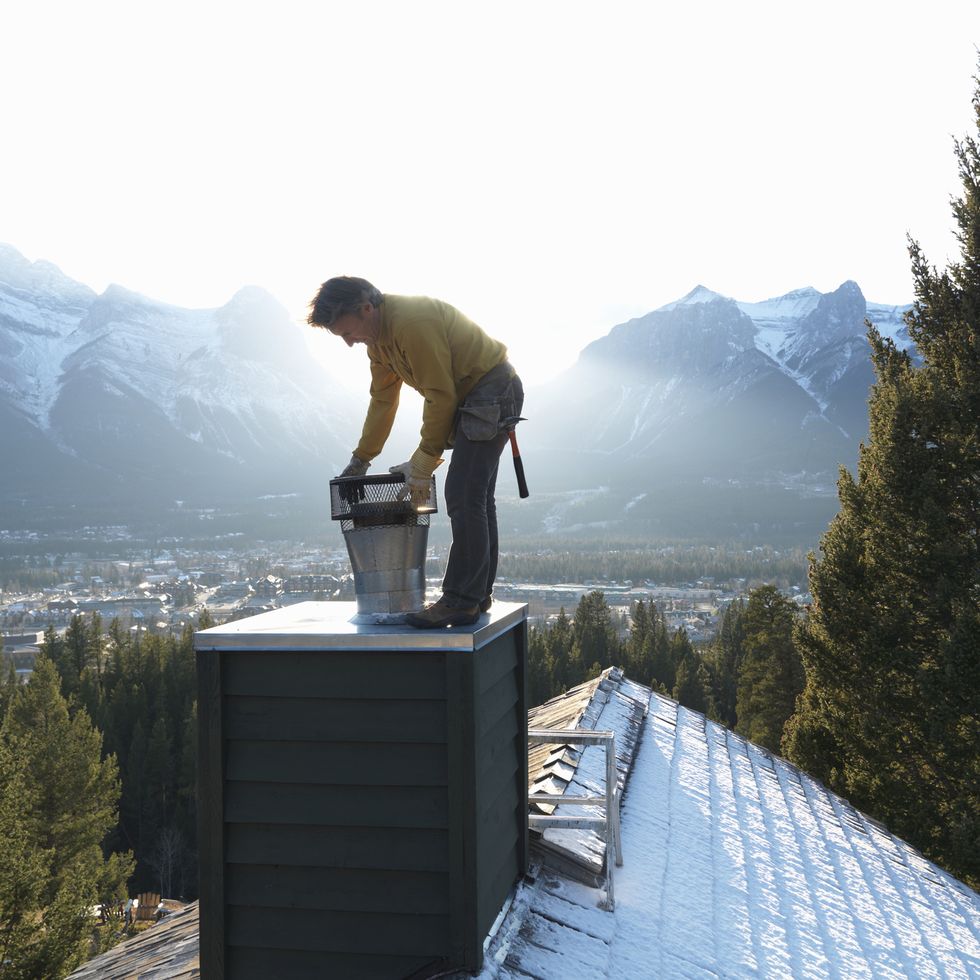 man adjusting chimney on snowy rooftop