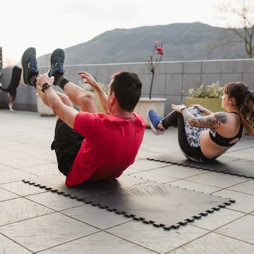 mature man and young woman doing crunches with sportswear on the terrace of his house at sunset
