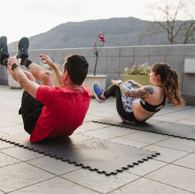 mature man and young woman doing crunches with sportswear on the terrace of his house at sunset