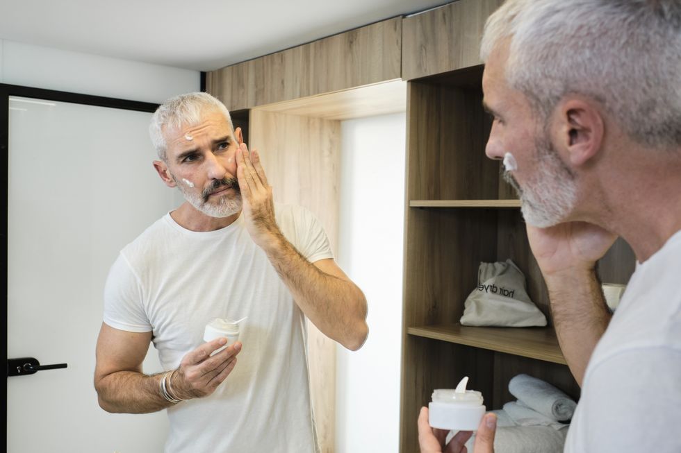 mature man applying face cream while looking in mirror at bathroom