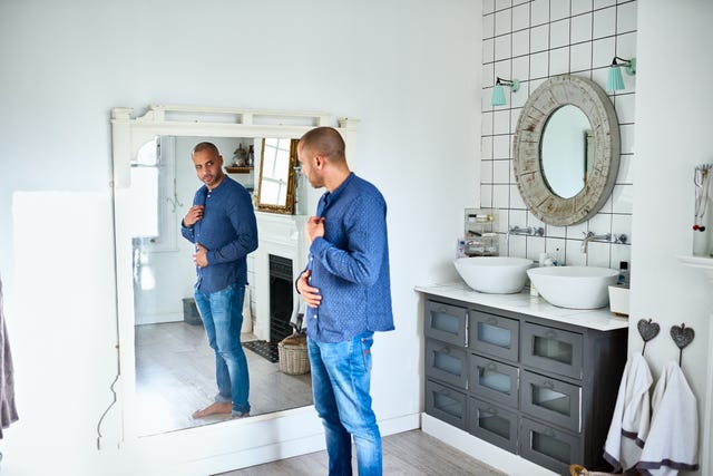 Ozempic lifestyle mature man checking himself in bathroom mirror and touching tummy