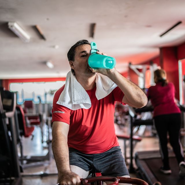 mature man using exercise bicycle and drinking water at a gym