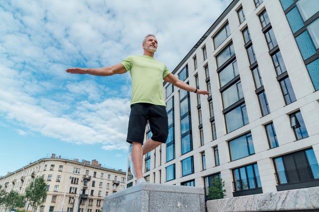 mature man with arms outstretched exercising on concrete by building