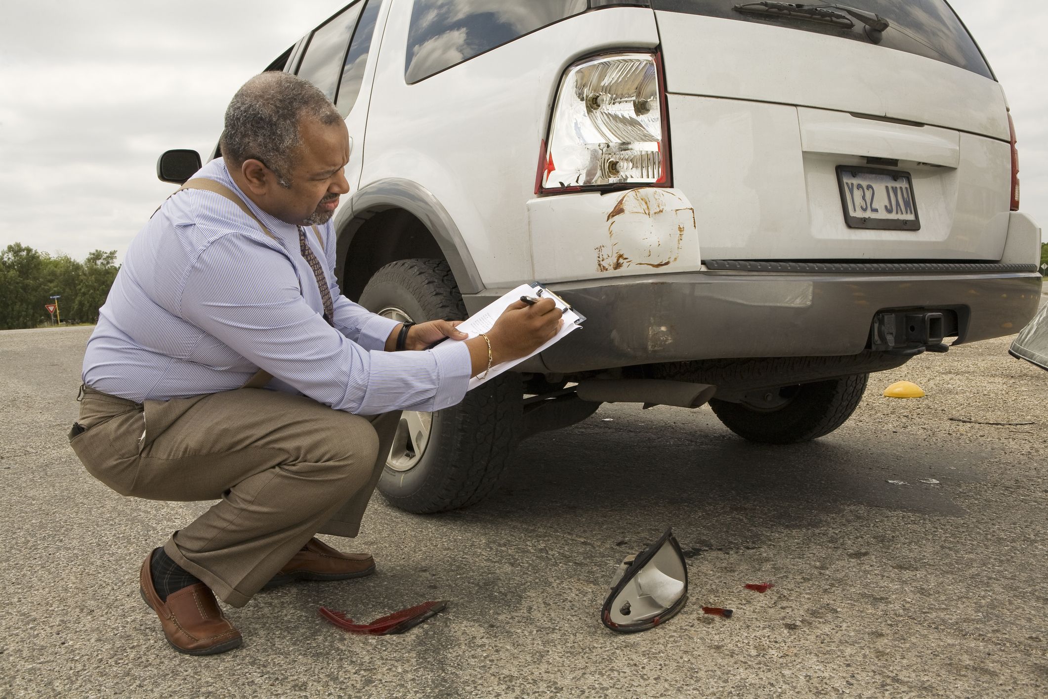 mature man writing on clipboard by crashed car