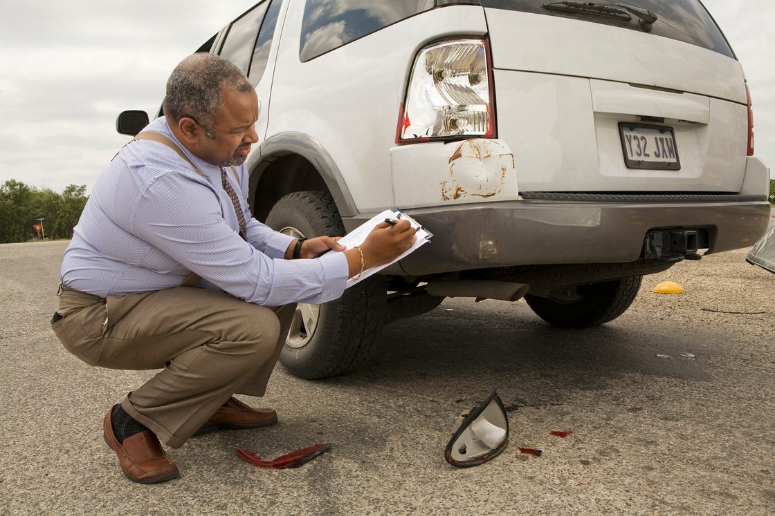 mature man writing on clipboard by crashed car