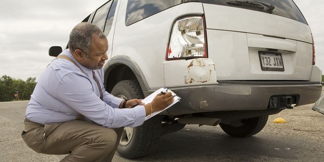 mature man writing on clipboard by crashed car