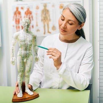 mature woman acupuncturist, doctor of traditional chinese medicine showing points on acupuncture model of human body