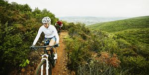mature woman climbing hill while riding mountain bike on trail with husband