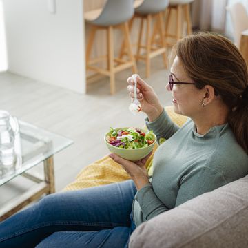 mature woman eating salad relaxed on sofa