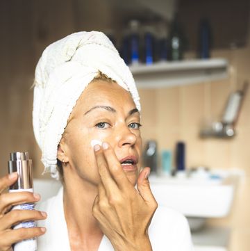 mature woman in bathrobe moisturizing face in bathroom