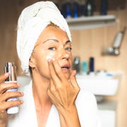 mature woman in bathrobe moisturizing face in bathroom