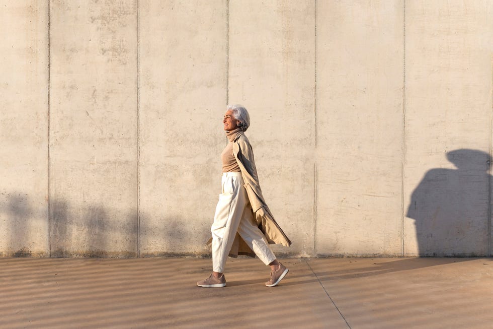 mature woman in trench coat walking on footpath