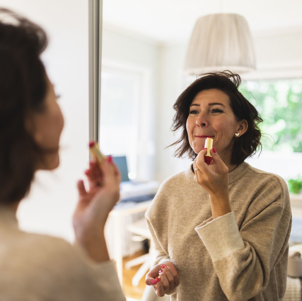 mature woman looking in mirror and applying lipstick