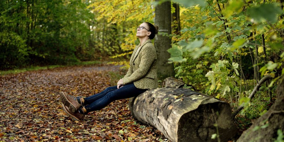 mature woman sitting on a tree trunk in a autumn forest
