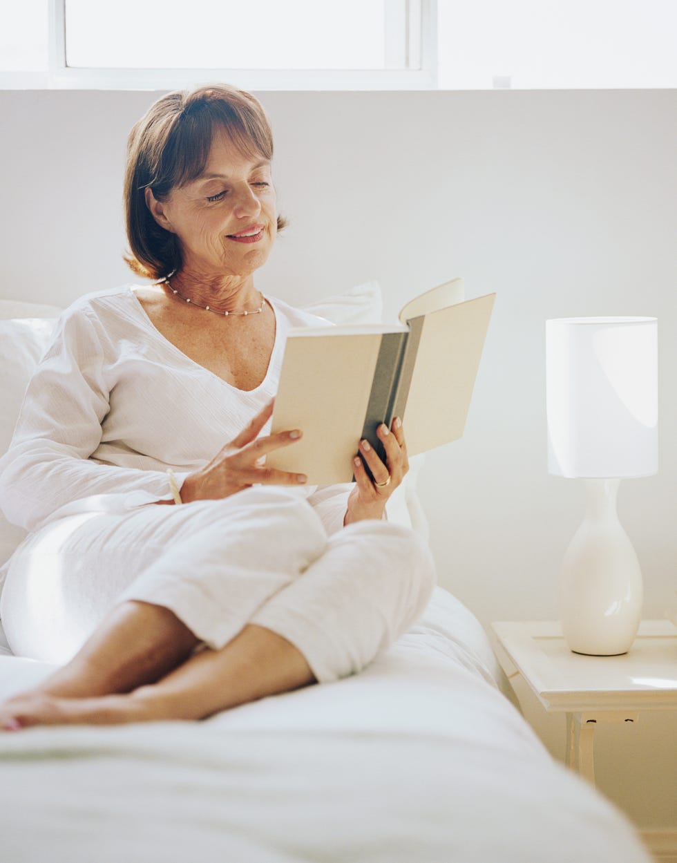 virtual happy hour ideas -  Mature woman sitting on bed, reading book