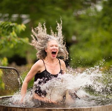 vrouw met grijs haar springt lachend in koud water