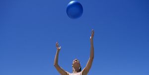 mature woman tossing fitness ball at beach