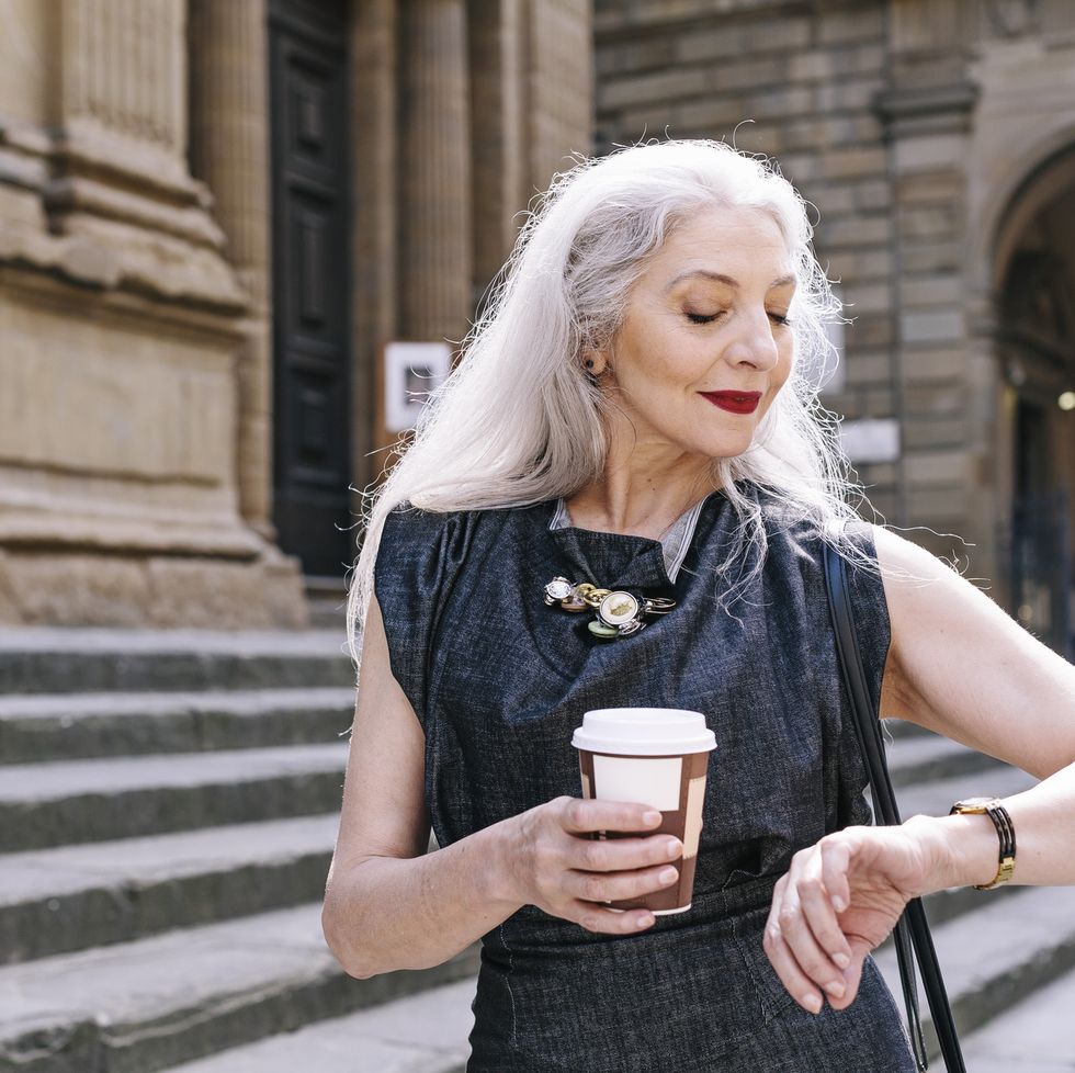 mature woman with long grey hair looking at wristwatch in florence, italy