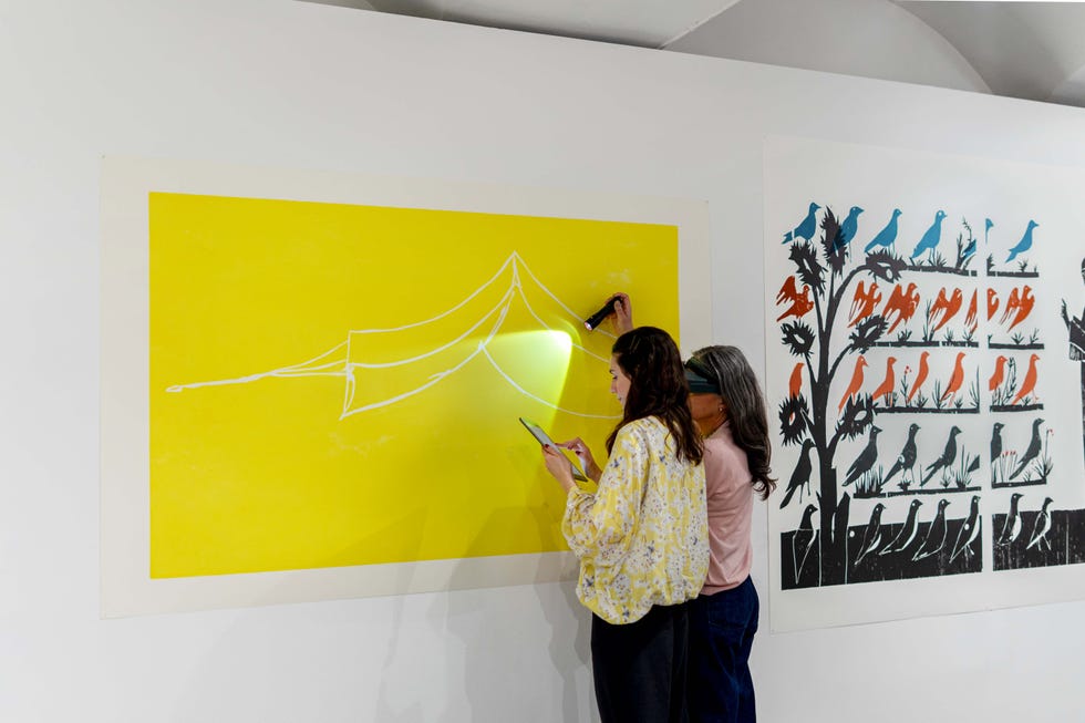 two individuals are drawing on a bright yellow wall while using a flashlight