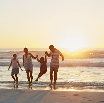 full length of parents with children enjoying vacation on beach during sunset