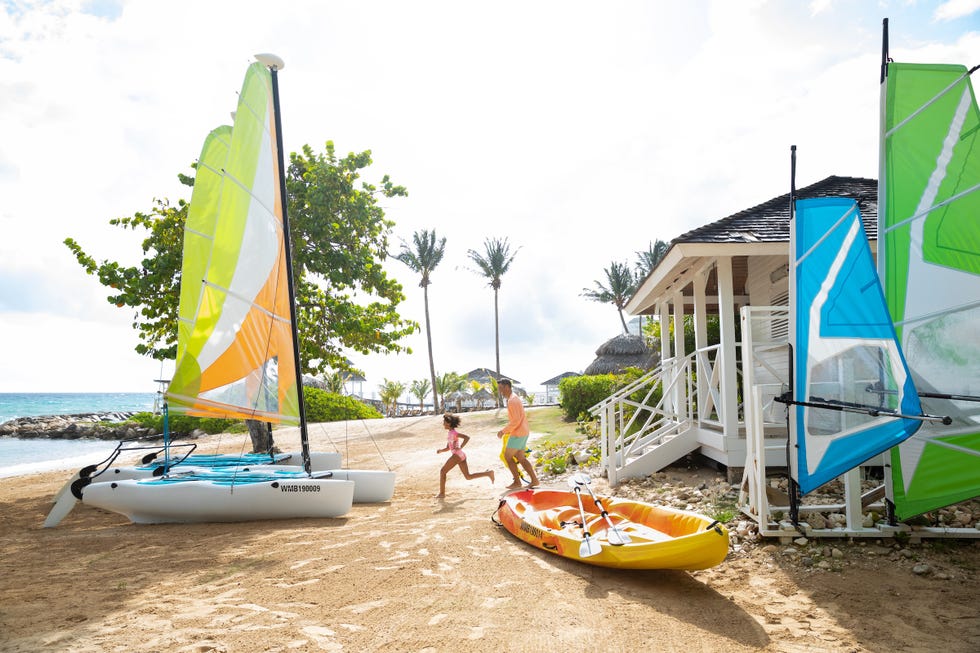 children playing on the beach with sailboats and a house in the background