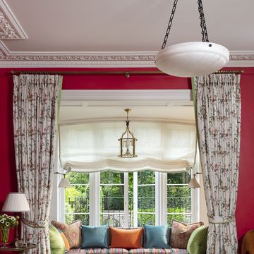 in the living room a convivial window seat overlooks an emerald and white back garden and a banquette has striped fabric