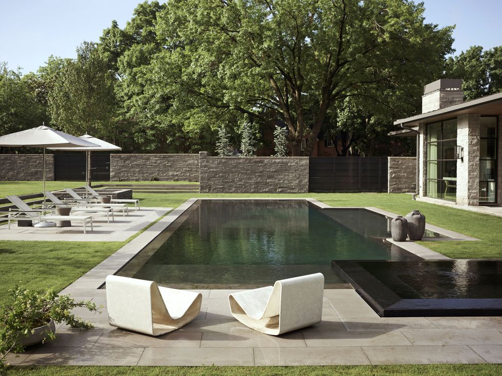 a pair of vintage loop chairs sit in front of a pool in a backyard
