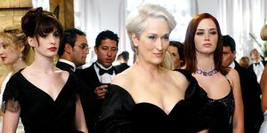 the devil wears prada film still featuring anne hathaway, meryl streep, and emily blunt in character all wearing formal black dresses at a cocktail party