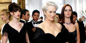 the devil wears prada film still featuring anne hathaway, meryl streep, and emily blunt in character all wearing formal black dresses at a cocktail party