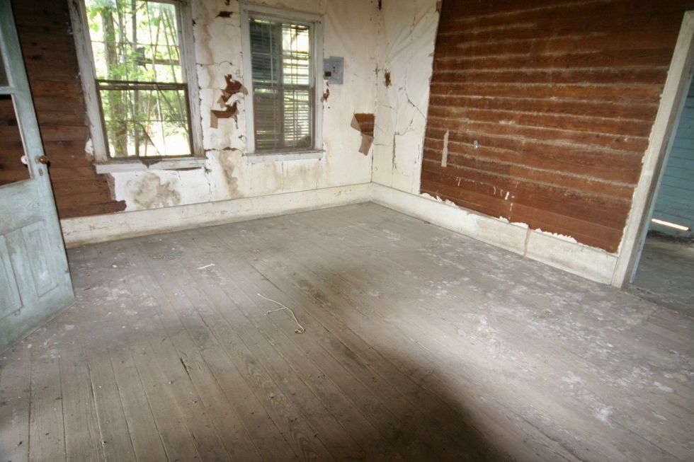 a rundown room with a wood floor and windows
