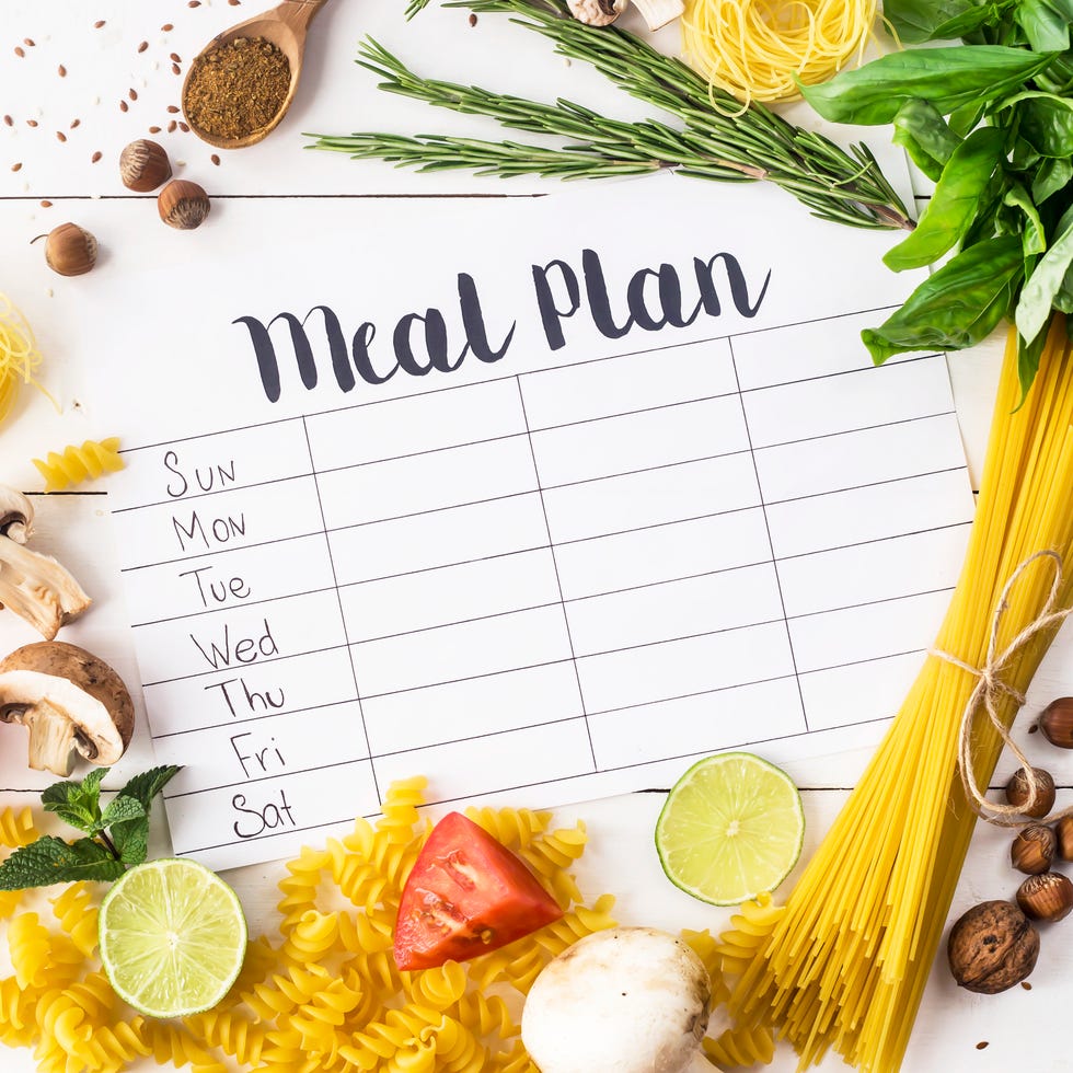 A meal plan for a week on a white table among products for cooking - pastas, basil, vegetables, lime, seeds, nuts and spices. Top view, flat lay, copyspace