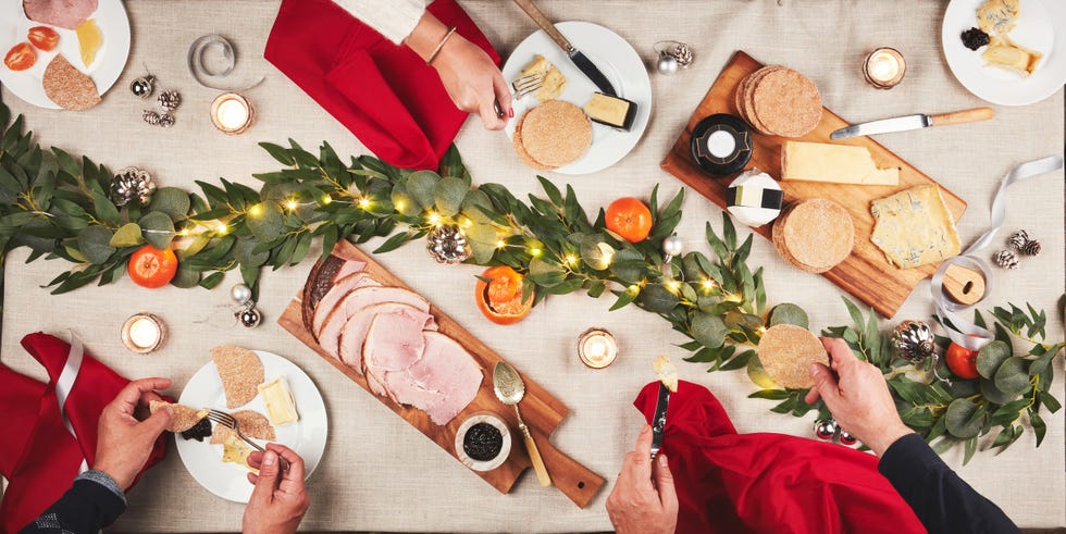 meat, charcuterie board and hands of people at table with christmas decoration for family celebration snack, high angle and platter with crackers, ham and cheese for starter at festive dinner party