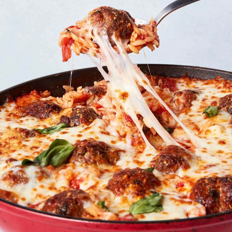 tomato based orzo in a skillet topped with meatballs and cheese