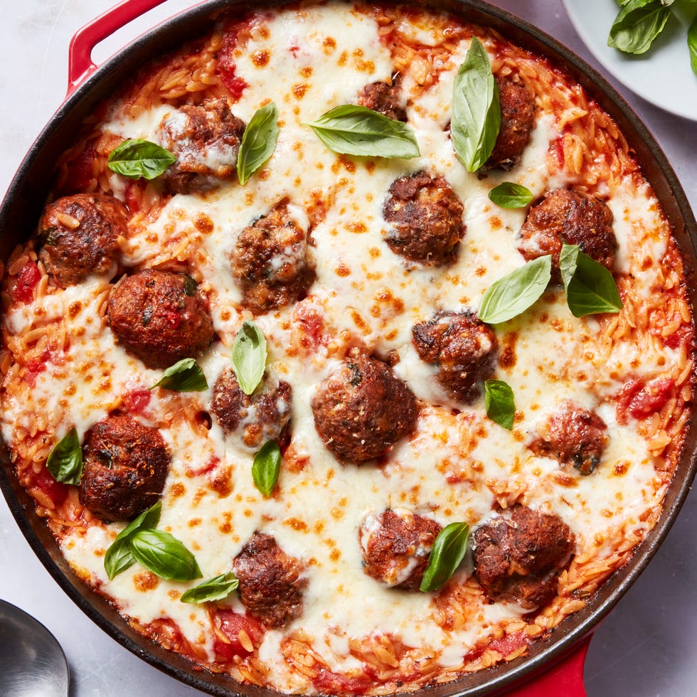 tomato based orzo in a skillet topped with meatballs and cheese