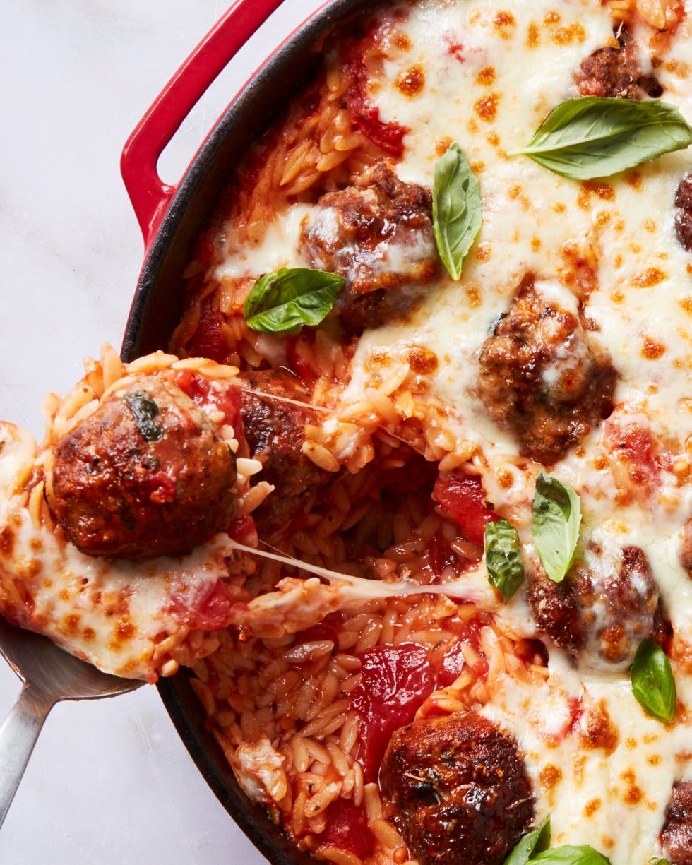 tomato based orzo in a skillet topped with meatballs and cheese