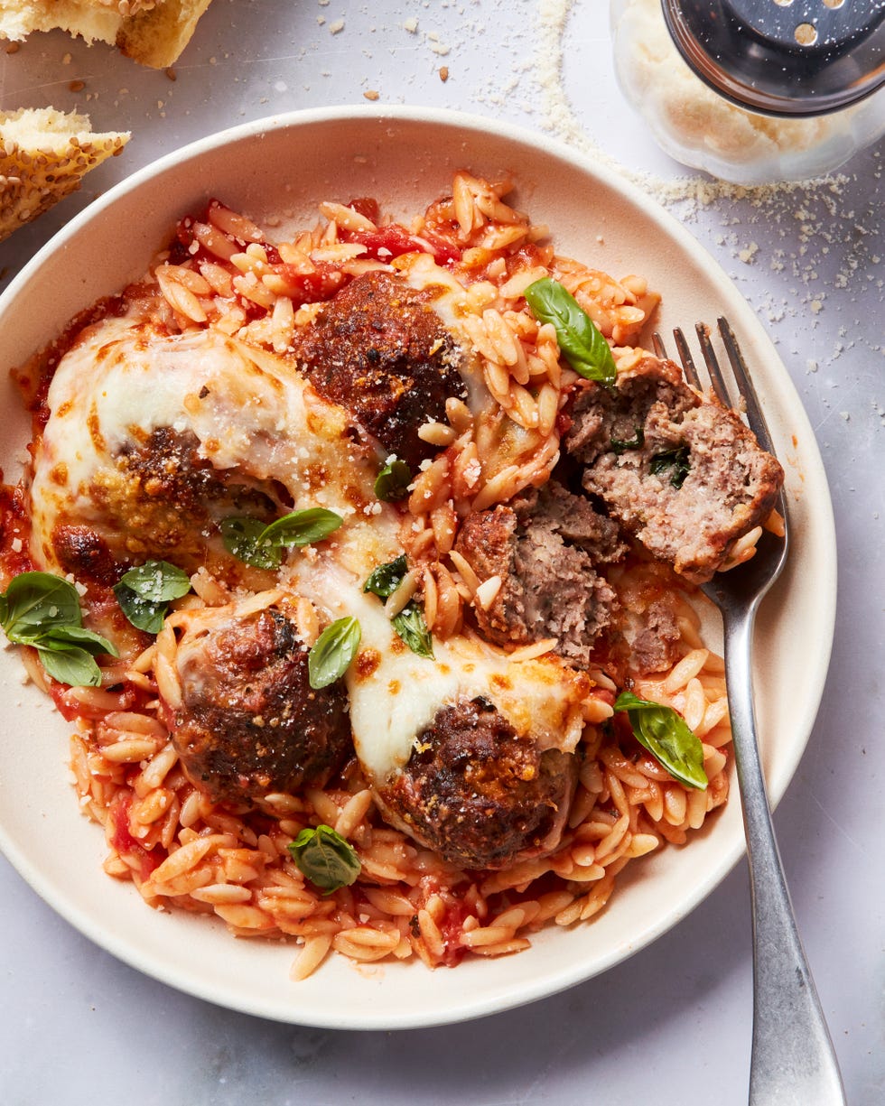 tomato based orzo in a skillet topped with meatballs and cheese