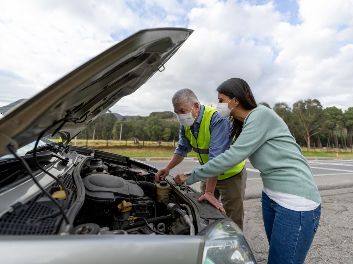 mechanic assisting woman having problems with her car on the road and wearing a facemask