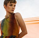 a person in a colorful dress stands against a backdrop of flowing orange fabric a person in a colorful dress stands against a backdrop of flowing orange fabric