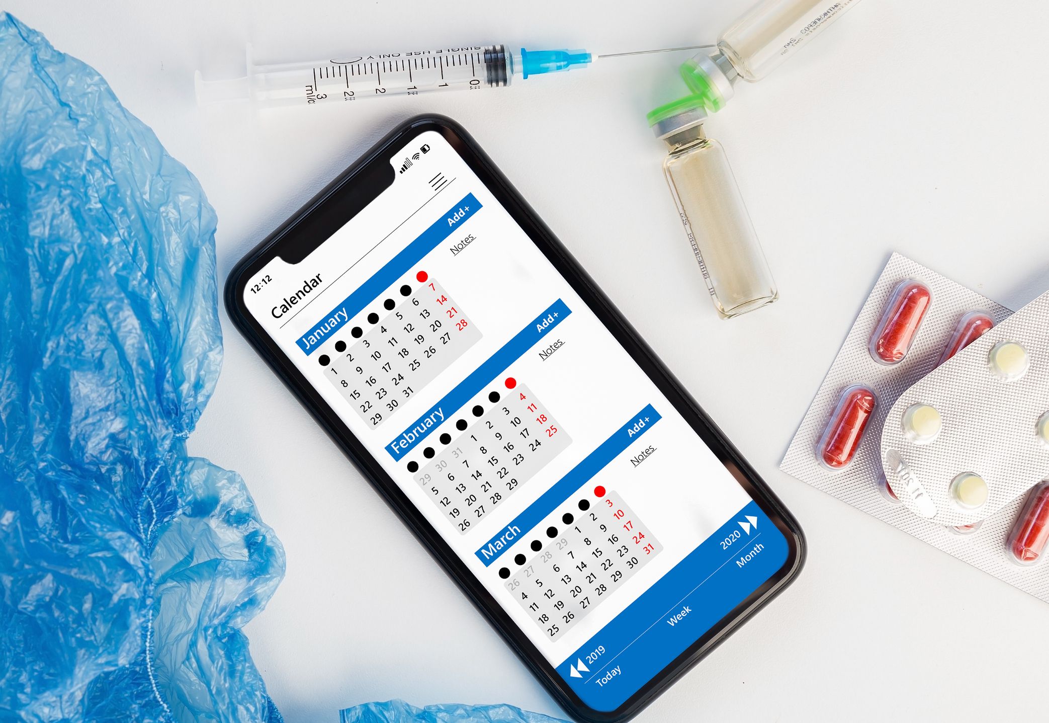 medical prescribing concept calendar on smartphone, syringe and pills top view