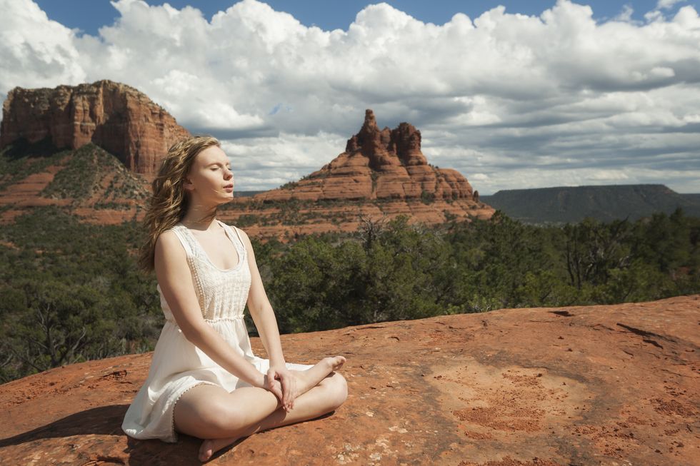 woman in meditating pose with legs crossed sitting on ground in front of beautiful red rock landscape