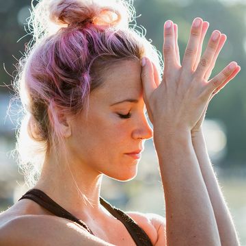 woman with pink hair and wearing workout clothes doing meditation outside