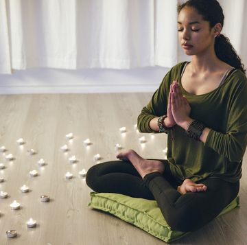 meditation cushions, best beautiful smiling mixed race teenage girl sitting on a green meditation cushion cross legged in prayer position with her eyes closed in a dim candlelit studio