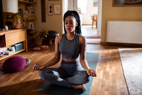 black woman sitting in a sunny room meditating in lotus pose