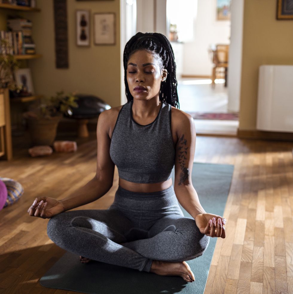black woman sitting in a sunny room meditating in lotus pose