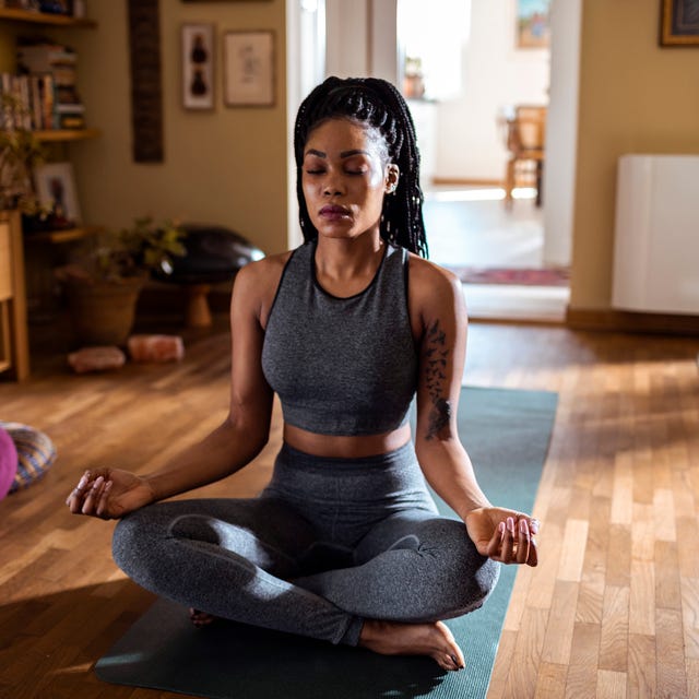 black woman sitting in a sunny room meditating in lotus pose